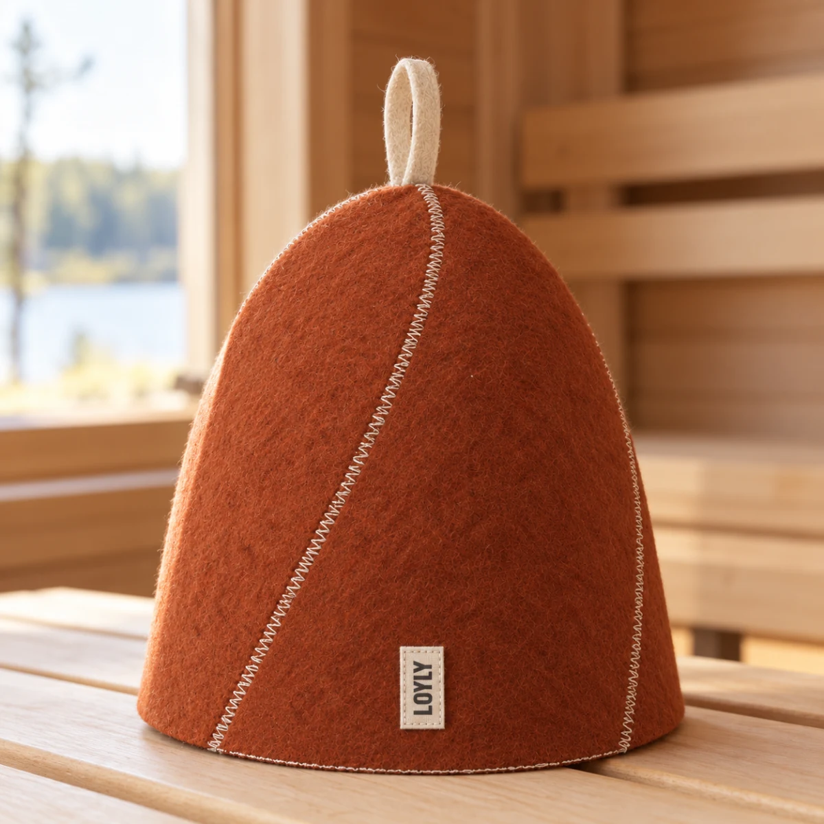Gorro Espiral Pinhão sobre um banco de sauna, com feltro de lã ferrugem, costura crua e alça no topo